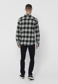 Camisa de franela a cuadros en negro y gris, de mangas largas, con puños abotonados, dobladillo curvado, combinada con pantalones negros y zapatillas negras.