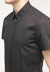 Czarna, krótka koszula z guzikami z gładkiego materiału, z tradycyjnym kołnierzykiem i dopasowanym krojem z subtelnym połyskiem.