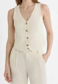 Beige linnen vest met een V-hals, vijf knopen en twee voorzakken; getailleerde pasvorm en gladde textuur. Gecombineerd met bijpassende broek.