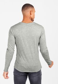 Graues Langarmshirt mit rundem Ausschnitt, weichem Material, taillierter Passform und sichtbaren Nähdetails an den Ärmeln und dem Saum.