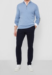 Ljusblå zip-tröja med lång ärm, i kombination med mörkblå chinos och vita sneakers, med en smal passform och mjukt material.