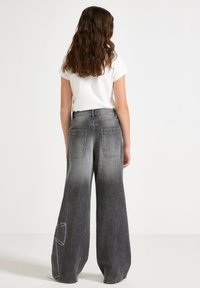 Szare dżinsy o szerokich nogawkach z efektem gradientu, z dużymi tylnymi kieszeniami i białymi detalami przeszycia, zestawione z gładką białą koszulką.