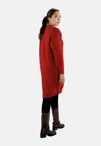 Rotes Strickkleid mit strukturierten Ballonärmeln, getragen über schwarzen Leggings und braunen kniehohen Stiefeln. Schlichte, übergroße Passform.