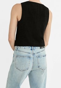 Czarny top bez rękawów z wysokim dekoltem, zestawiony z jasnoniebieskimi dżinsami z wysokim stanem o klasycznym pięcio-kieszeniowym kroju.