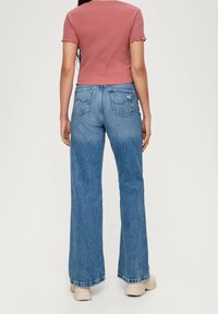 Lyserød kortærmet crop top med flagrende kant, parret med højtaljede blå jeans med en afslappet pasform og synlige baglommer.