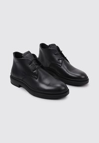 Botas de tobillo de cuero negro con un acabado suave, que presentan una puntera redondeada, costuras sutiles y dos cordones en la parte delantera. Suelas de goma planas.