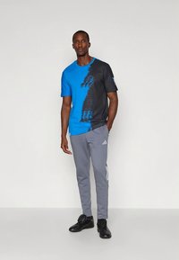 Modré a čierne tričko s digitálnym vzorom, doplnené sivými teplákmi s bielymi pruhmi a logom. Čierne tenisky.