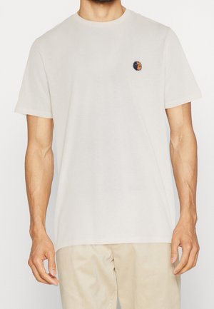 Lysebeige bomulds-T-shirt med korte ærmer, rund halsudskæring og et lille broderet solmotiv på venstre bryst.