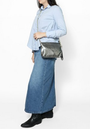 Sac en bandoulière en argent métallique avec un design d'enveloppe, présentant une surface texturée et une chaîne pour l'épaule, posé contre une chemise bleu clair.