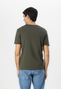 Camiseta de manga corta verde oscuro hecha de algodón, con cuello redondo y un corte holgado, combinada con jeans de mezclilla azul claro.