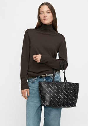 Zwarte tote bag met witte logoprint, glad synthetisch materiaal, rechthoekige vorm, dubbele handvatten, gecombineerd met een bruine coltrui en denim.