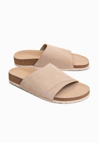 Paire de sandales slides en daim beige avec larges brides et semelles effet liège sur fond blanc.