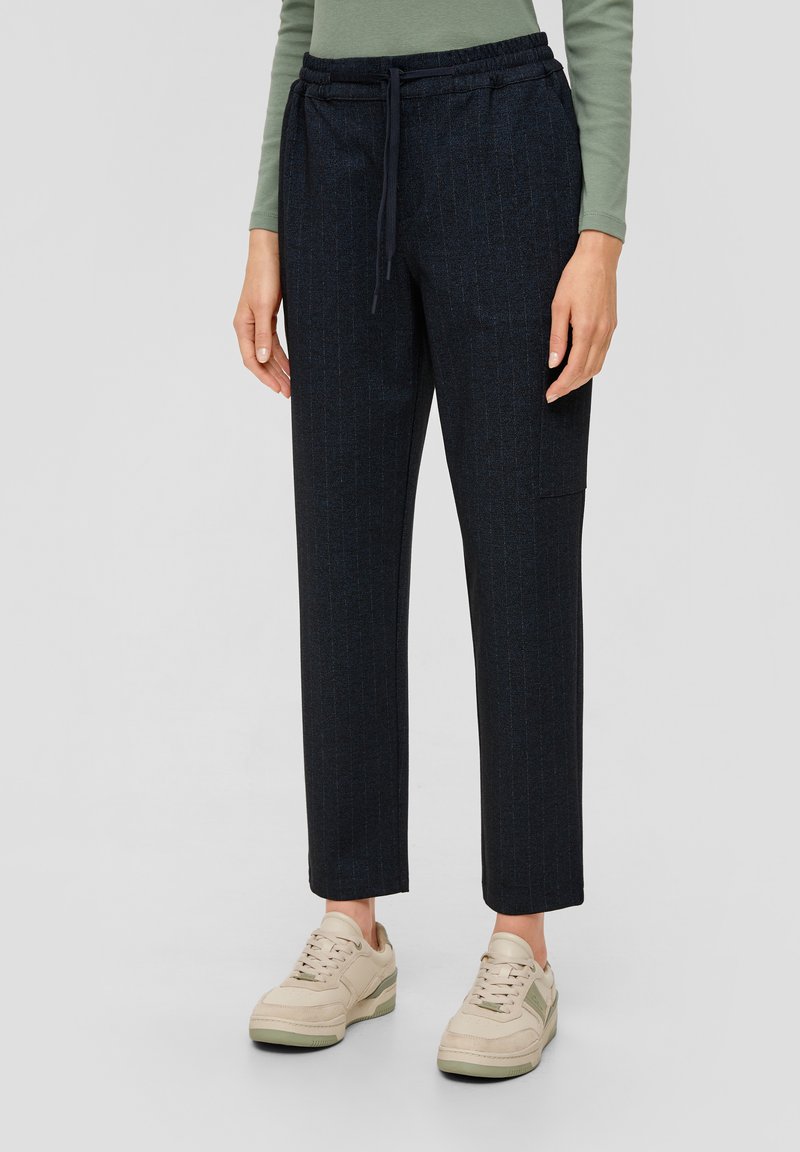Marineblauwe pantalon met streepjes, voorzien van een elastische tailleband en voorkruiszakken, gecombineerd met lichtgekleurde sneakers. Geverfde stof met een getailleerde pasvorm.