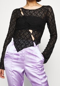 Black lace long-sleeve top featuring cut-out and ruffled details, paired with high-waisted, shiny lavender satin pants.