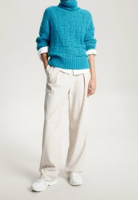 Turkis strikket turtleneck sweater med et tekstureret mønster, parret med cremefarvede brede bukser og hvide sneakers.