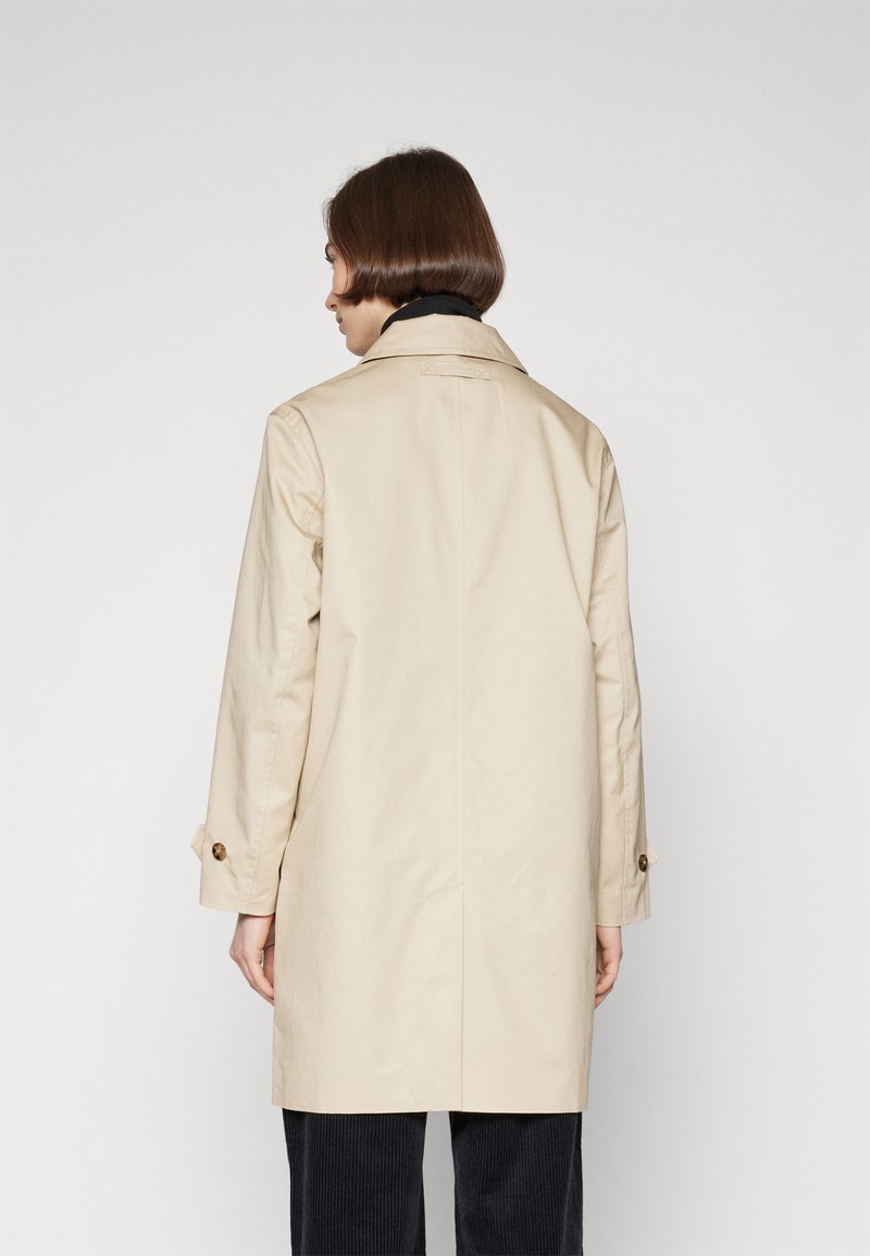 Gabán beige con diseño de doble botonadura, detalles de botones en las mangas y un cuello clásico, confeccionado en una tela suave.