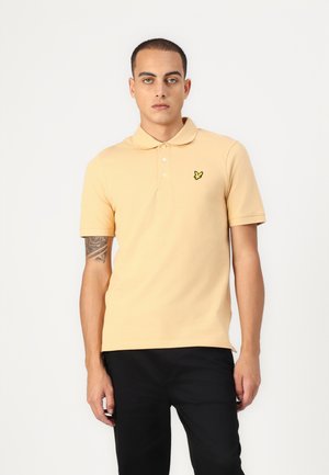 Šviesiai oranžinė polo marškinėliai, pagaminti iš medvilnės, su trimis mygtukais, trumpomis rankovėmis ir mažu, geltonu siuvinėtu logotipu ant krūtinės.