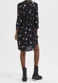 Vestido negro con un patrón floral en púrpura y blanco, con mangas largas, una cintura elástica y un dobladillo curvado. Combinado con botas negras de tobillo.