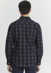 Camisa de manga larga azul marino con un patrón de cuadrícula blanca, cuello abotonado y dobladillo curvado. La tela es suave y tiene un ajuste estructurado.