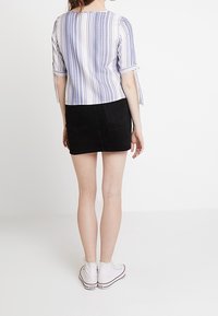 Pasiasty bawełniany top w białym i niebieskim kolorze, zestawiony z czarną dżinsową spódnicą mini. Białe trampki dopełniają stylizację. Widoczne detale rękawów i hemu.