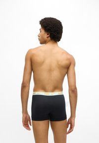 Meeste mustad bokserid, mille vöökohal on heleroosa ja kollane Nike logo, istuva lõike ja siledat tekstuuriga.