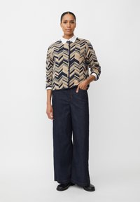 Cardigan cremoso e blu notte con motivo a zigzag e colletto bianco, abbinato a pantaloni a gamba larga in jeans scuri e scarpe nere.