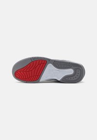 Semelle d’une chaussure de sport avec une semelle en caoutchouc grise, blanche et rouge, montrant des motifs texturés et le logo Nike Air au centre.