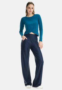 Teal long-sleeve top with a cropped design and navy wide-leg pants featuring side pockets, both made of a smooth, stretchy fabric.