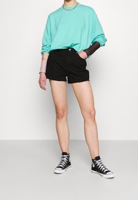 Felpa turchese, pantaloni shorts in denim neri e sneaker alte nere con suola bianca. I pantaloni shorts hanno l'orlo sfilacciato.
