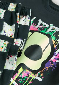 Sort sweatshirt og bukser med et neongrønt dødhoved grafisk design, pyntet med livlige malerpletter i pink, lilla og orange. Blød tekstur.