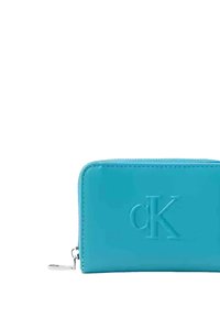 Portafoglio in pelle sintetica turchese con logo "CK" in rilievo, chiusura con zip, forma rettangolare, texture liscia e dettagli in metallo color argento.