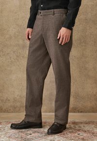 Brown, textured trousers with a straight leg design, featuring a button closure and side pockets, paired with black loafers.