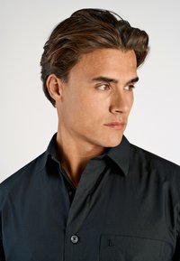 Zwarte overhemd met knoopsluiting en een zak, voorzien van een geborduurd "L", gemaakt van een soepele stof, gestructureerde kraag en slim fit ontwerp.