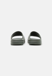 Zelene gumene sandale na slip-on s otvorenim petom, sa teksturiranom podlogom i glatkim gornjim dijelom, pokazujući minimalistički dizajn.