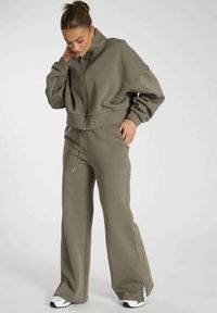 Olijf groene cropped sweatshirt met hoge kraag en rits, gecombineerd met loszittende sweatpants. Zachte textuur en ontspannen ontwerp.