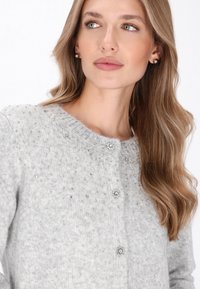 Grauer Strickcardigan mit Rundhalsausschnitt, Juwelenakzenten und drei dekorativen Knöpfen. Weicher Textur mit einem subtilen Muster.
