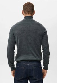 Pulover tricotat de culoare gri închis, cu mâneci lungi, guler înalt și o textură moale. Purtați cu blugi din denim închis, văzut din spate.