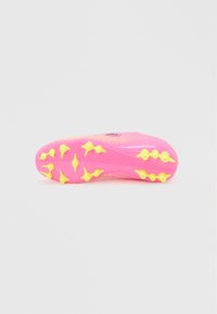 Φωτεινή ροζ σόλα ποδοσφαιρικού παπουτσιού με κίτρινες τάπες διατεταγμένες για πρόσφυση σε σκληρές επιφάνειες.