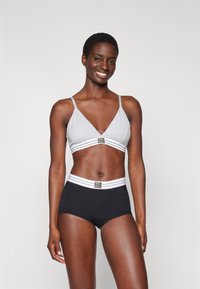 Bralette gris clair avec des fines sangles et une bande rayée blanche ; associée à un shorty noir avec une taille rayée blanche.
