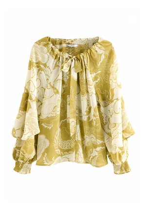 Żółto-kremowa bluzka we wzory z wiązaniem z przodu, luźnym krojem i szerokimi rękawami, zestawiona z niebieskimi, wysokim stanem, prostymi jeansami oraz brązowymi botkami.