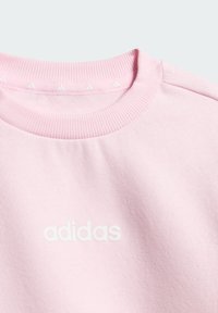 Svijetloružičasta majica s okruglim izrezom i bijelim Adidas logotipom u središtu prsa te malim Adidas logotipima na unutarnjem rubu ovratnika.