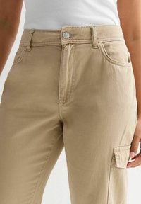 Khaaki spodnie cargo z wysokim stanem, zapięcie na guzik i kieszeniami bocznymi. Wykonane z miękkiej, wytrzymałej bawełny o gładkiej fakturze.