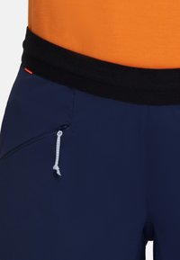 Marinblå shorts med svart midjeband, utrustade med en dragkedjeficka och en snöre. Designen inkluderar en stark orange detalj.