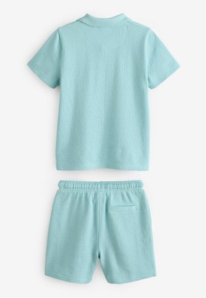 Hellsblaue gestrickte Polohemd mit kurzen Ärmeln und geripptem Kragen, kombiniert mit Shorts mit elastischem Bund und einer Gesäßtasche. Strukturmuster auf dem gesamten Kleidungsstück.