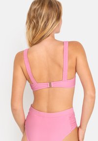 Ružový bikiny top s širokými, štruktúrovanými ramienkami a zapínaním na chrbte. Hladká tkanina s jednoduchou, jednofarebnou úpravou a minimálnym zdobením.