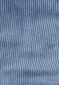 Tissu en velours côtelé bleu avec une texture verticale et côtelée, offrant une surface douce et moelleuse. La texture est lisse avec des nervures fines et uniformément espacées.