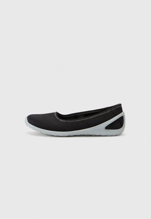 Black flat shoe with a rounded toe, elastic opening, gray rubber sole, and contrasting stitching along the upper edge. Minimalistic design.