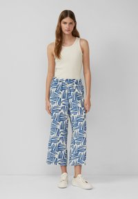 Witte geribde tanktop gecombineerd met blauw-witte gewatteerde wijde broek. Heeft een losse pasvorm en een elastische tailleband. Draagt met witte sneakers.