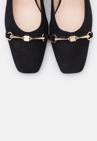 Černé semišové baleríny se čtveratou špičkou, se zlatě tónovaným řetízkem jako ozdobou a čtvercovým zapínáním vpředu. Hladká podšívka.