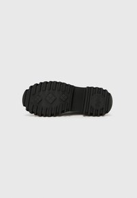 Black rubber shoe sole with textured grip patterns and a circular logo. Features ridged edges and a thick, durable design for traction.